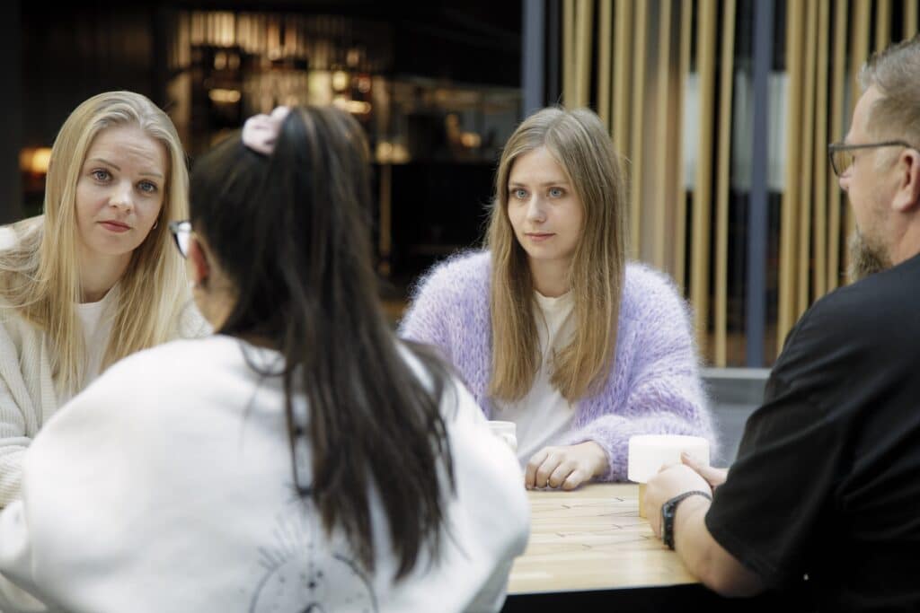 Bildet som viser en gruppe personer som sitter rundt et bord og prater med hverandre. To sitter med ryggen til kamera.