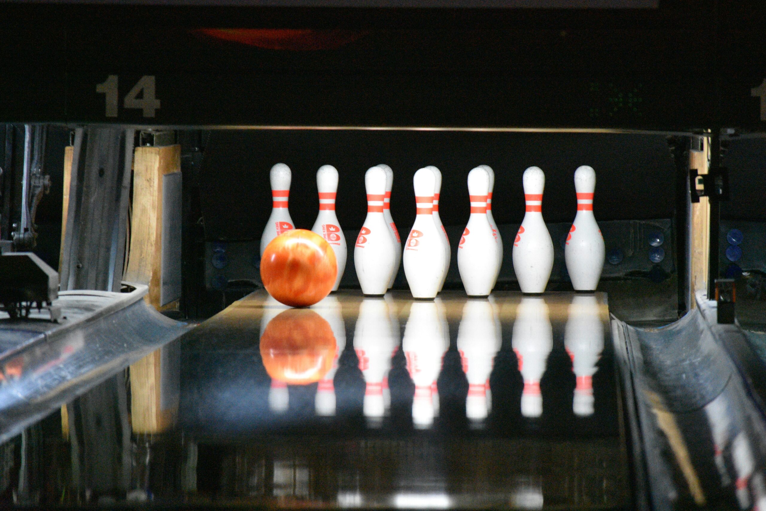 En bowlingball ruller mot en gruppe kjegler i en bowlingbane, klare til å bli slått ned. Refleksjoner på banen gir bildet en dynamisk følelse.