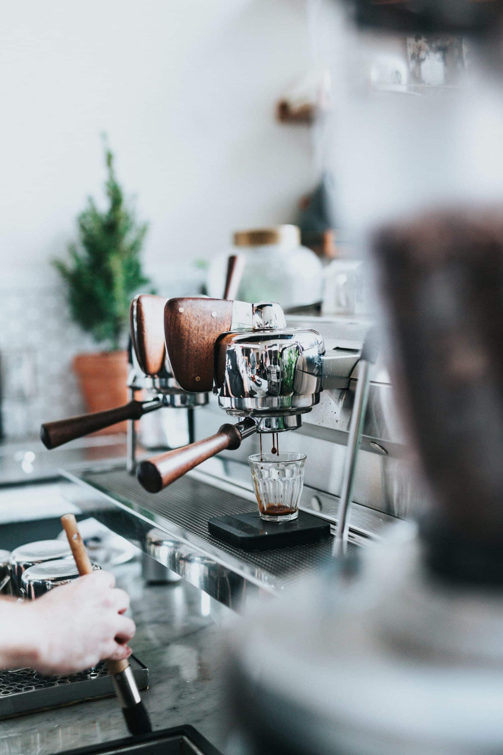 En espressomaskin i en moderne kaffebar, med håndtakene klare til å lage kaffe. Bildet er lyst og viser et innbydende kaffemiljø.