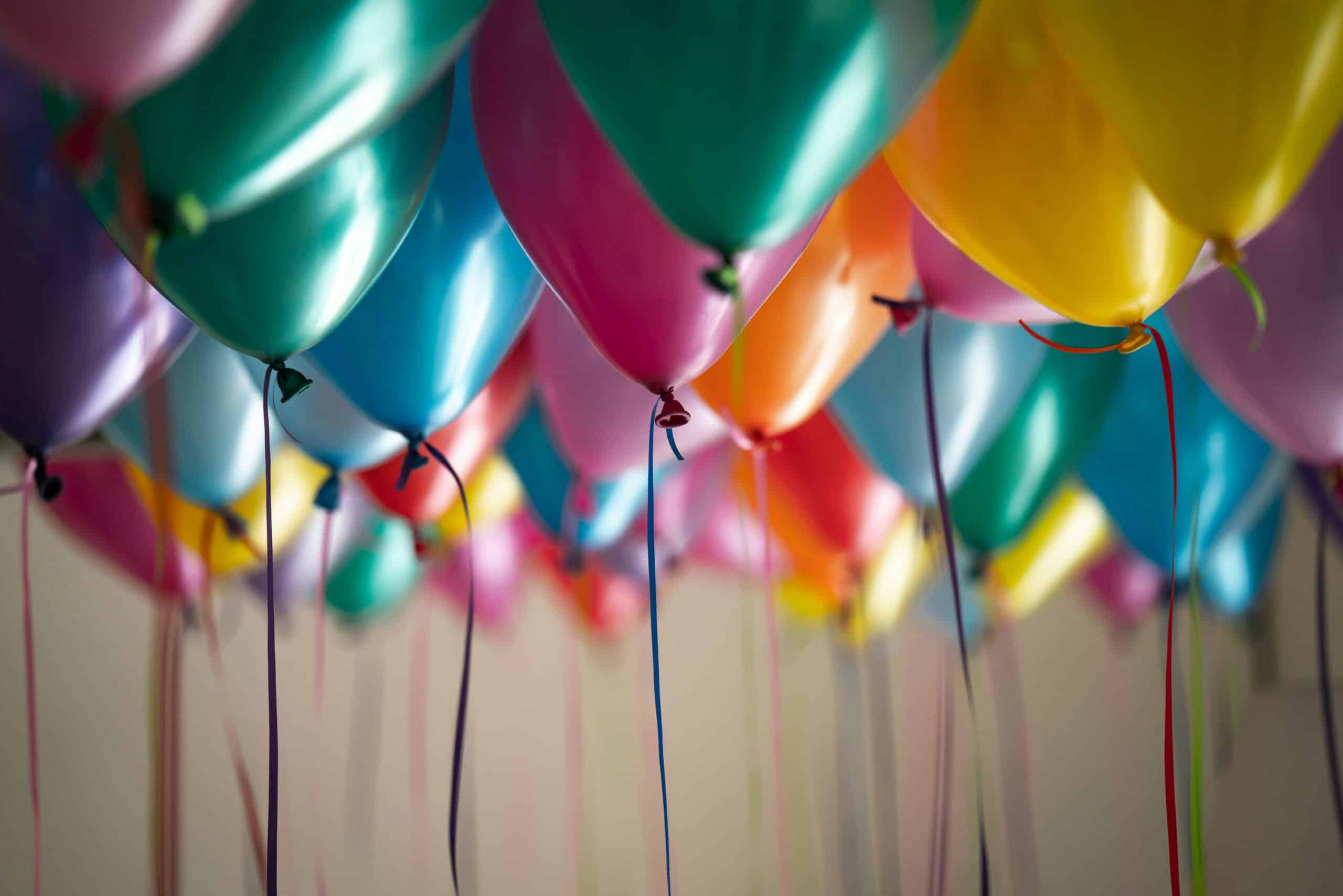 Fargerike ballonger henger tett sammen, hver med snorer som henger nedover. Bildet har en festlig og gledelig atmosfære.