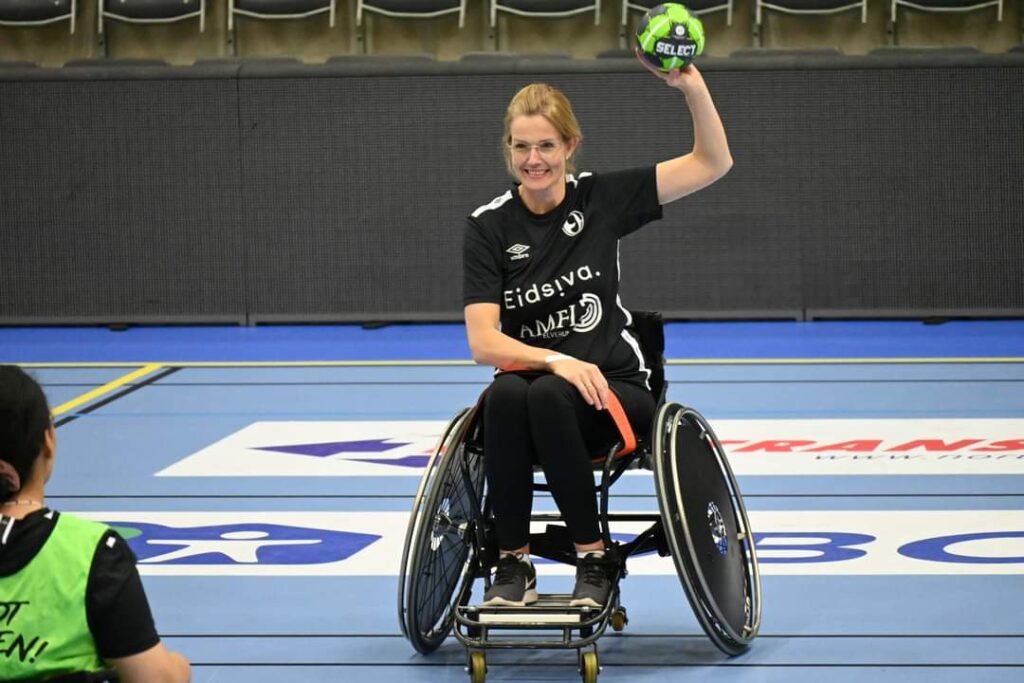 Bilde som viser Camilla Snestad Wærhaug på håndballbanen. Hun sitter i en rullestol og holder en ball i hånden. 
