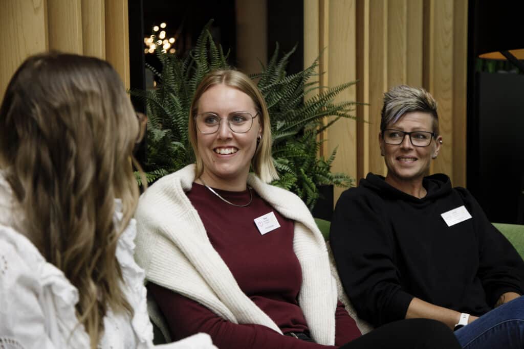 Tre jenter som sitter og prater med hverandre på konferanse.