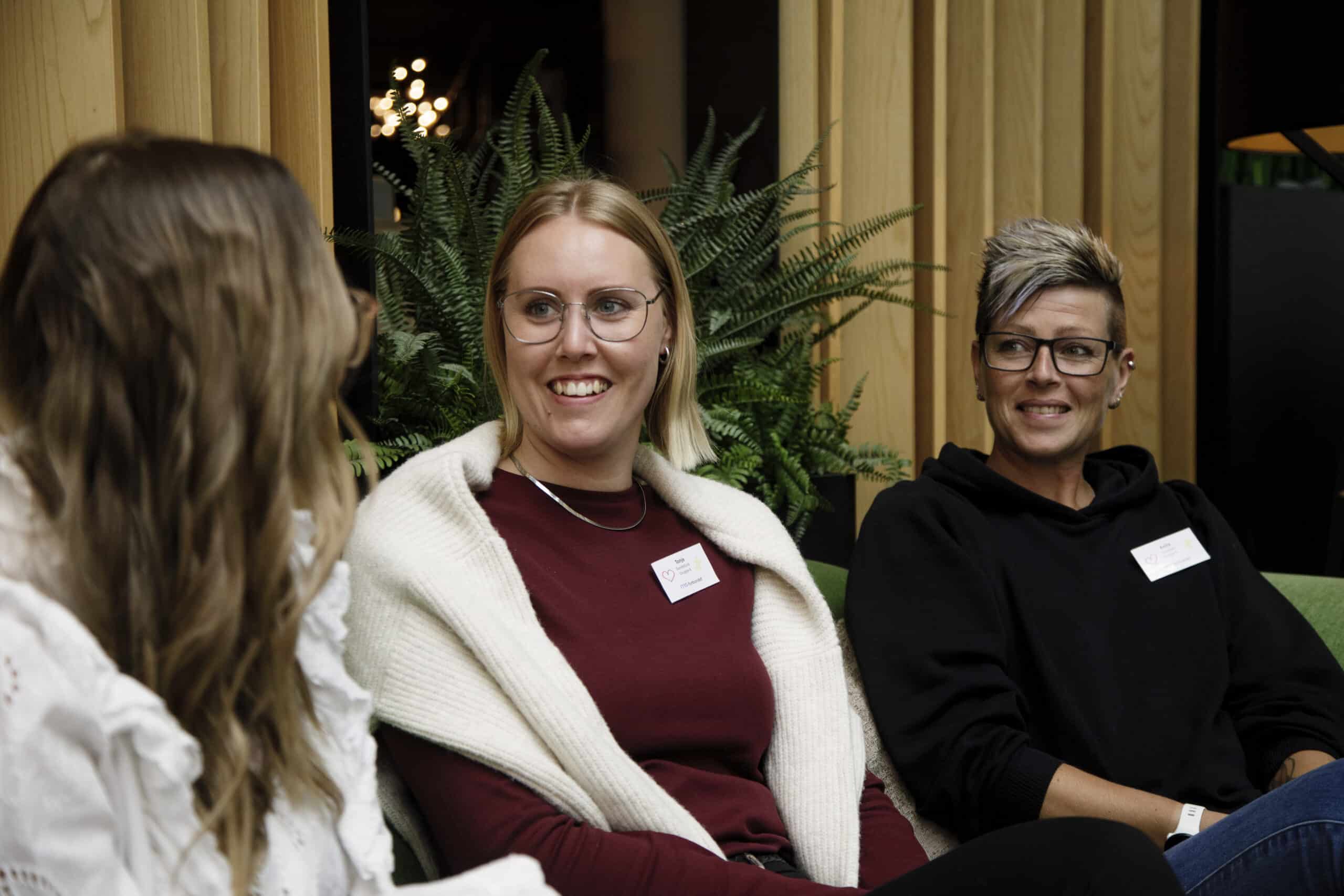 Tre jenter som sitter og prater med hverandre på konferanse.