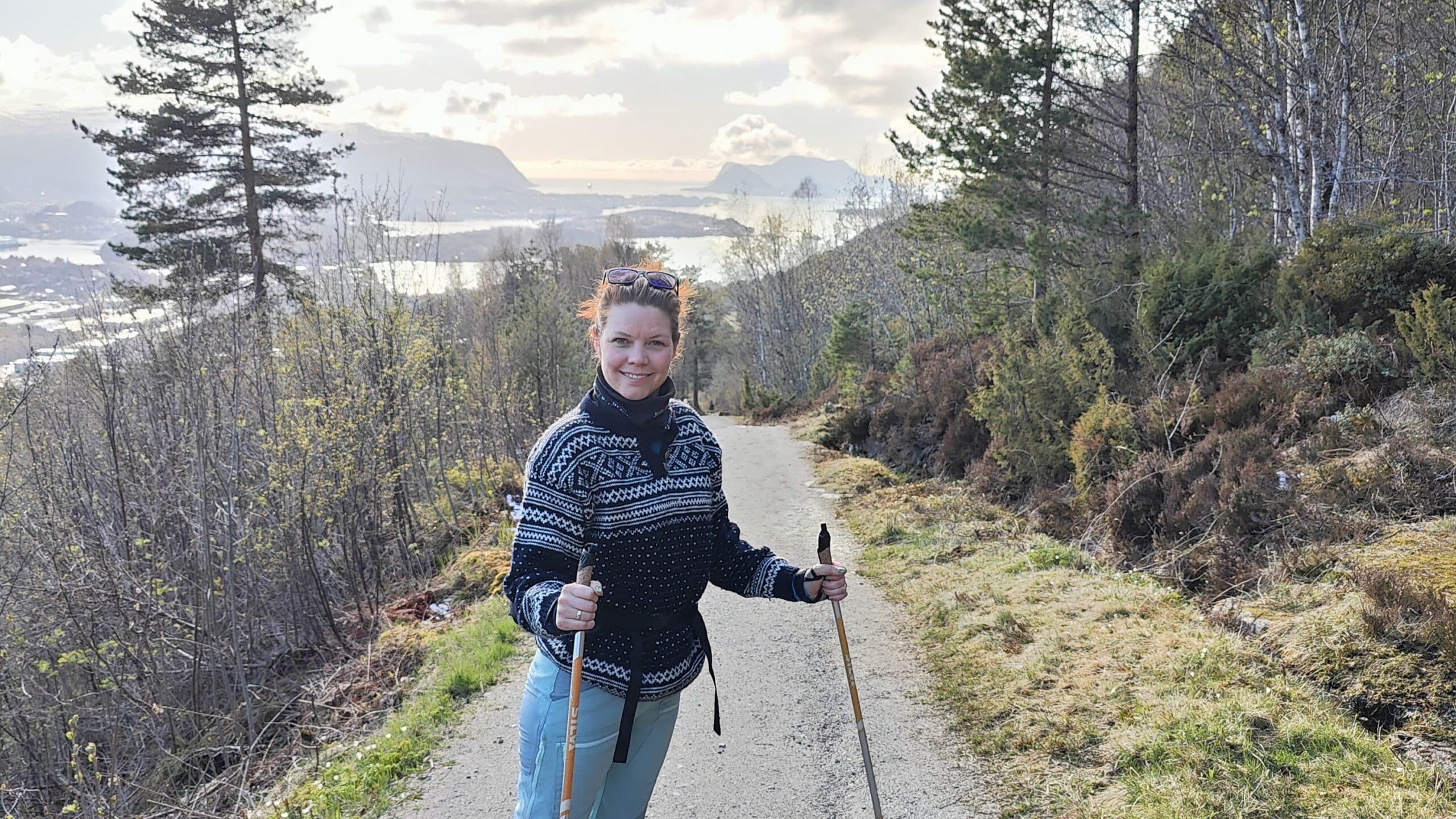 Bilde av Annette Madsen Arnestad som står på en tursti med utsikt over fjord og fjell.