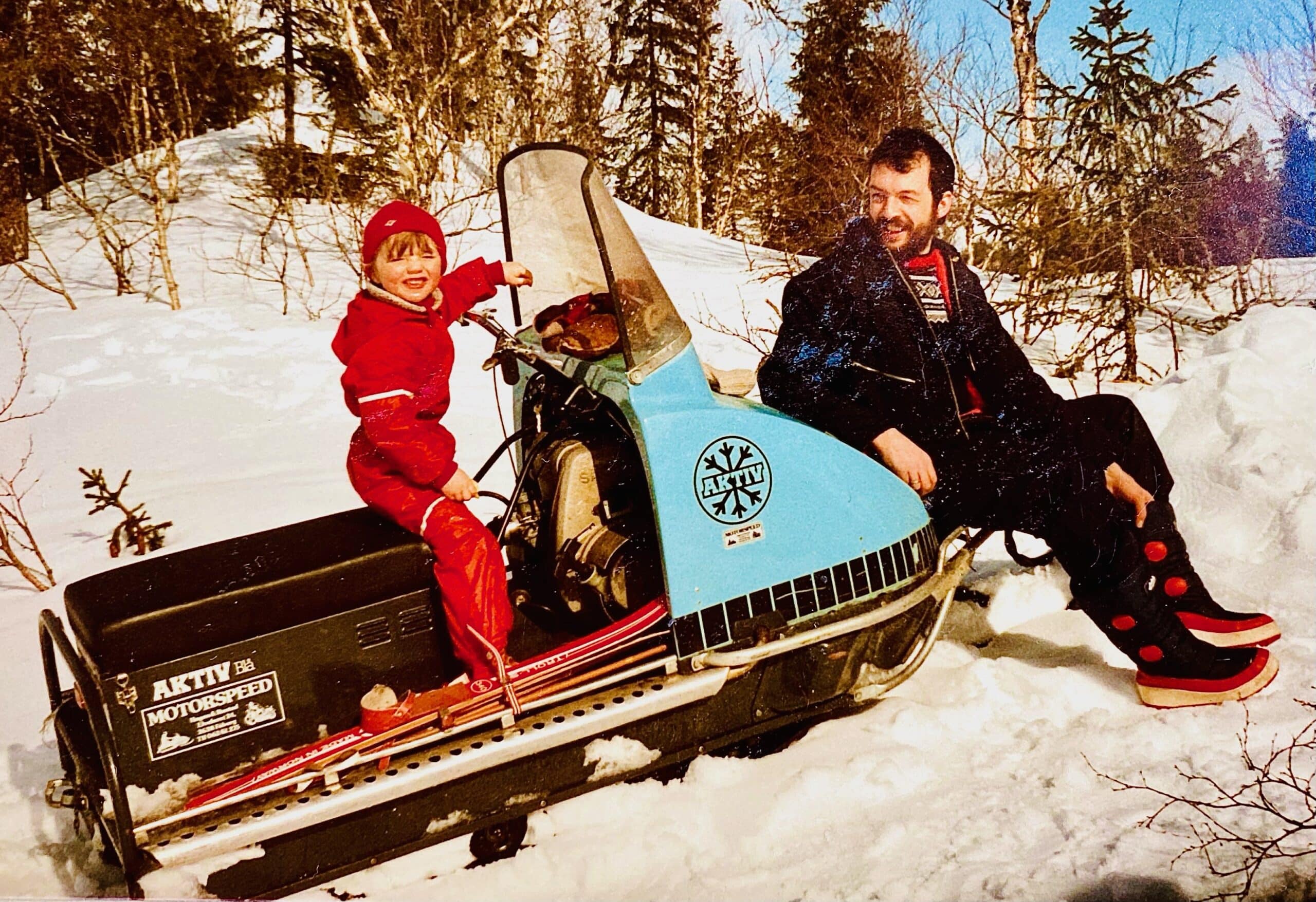 Bilde av Eirik som liten gutt. Han sitter på en snøscooter. Foran scooteren sitter faren Ketil.