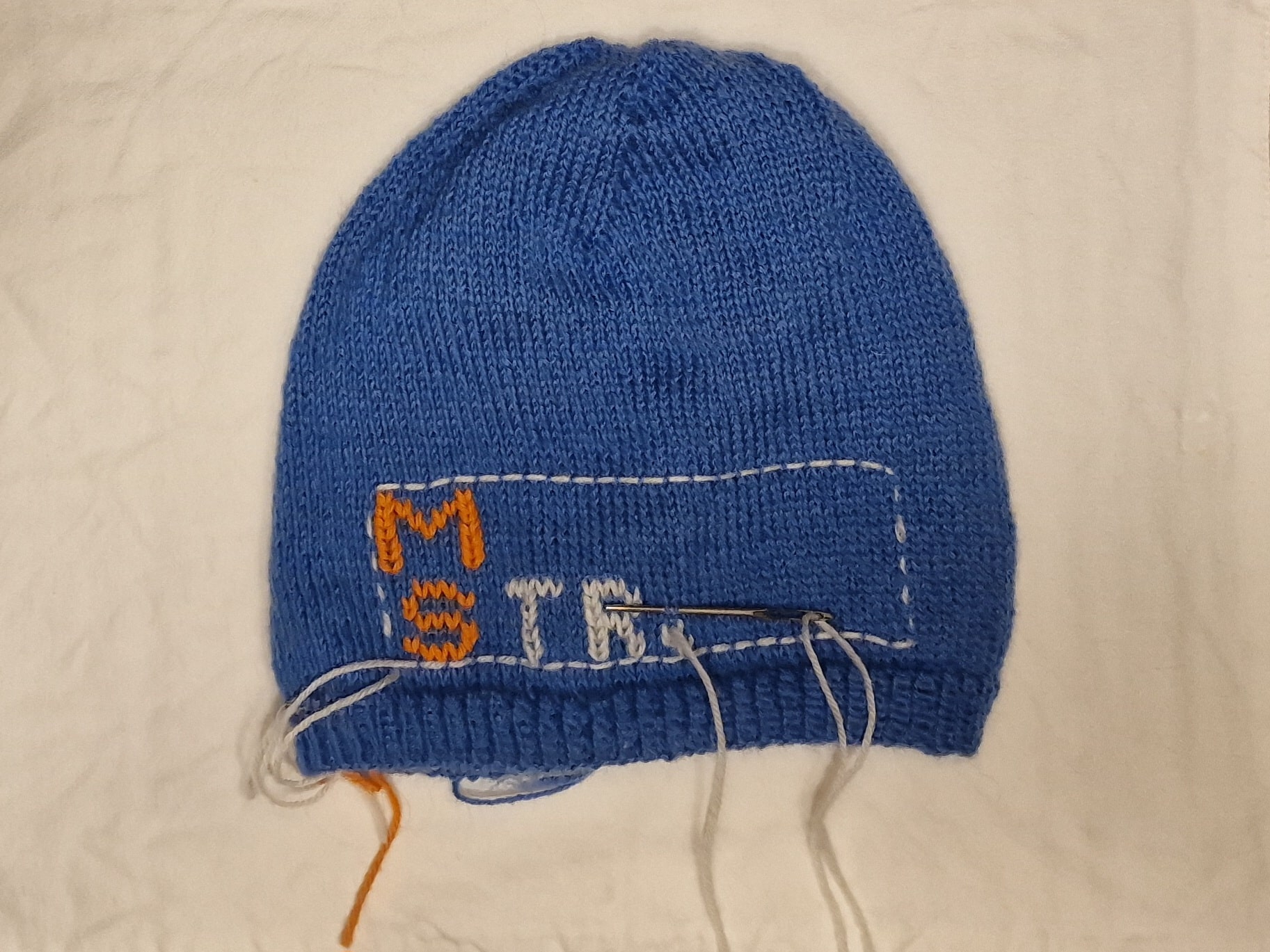 Bilde av en blå strikket lue. Det er brodert inn MS på den. Strikk for MS: