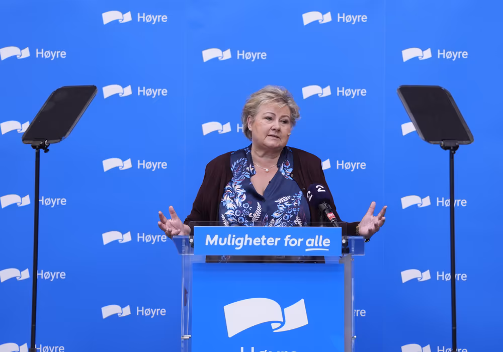 Bilde av Erna Solberg på pressekonferanse foran høyre-logoen
