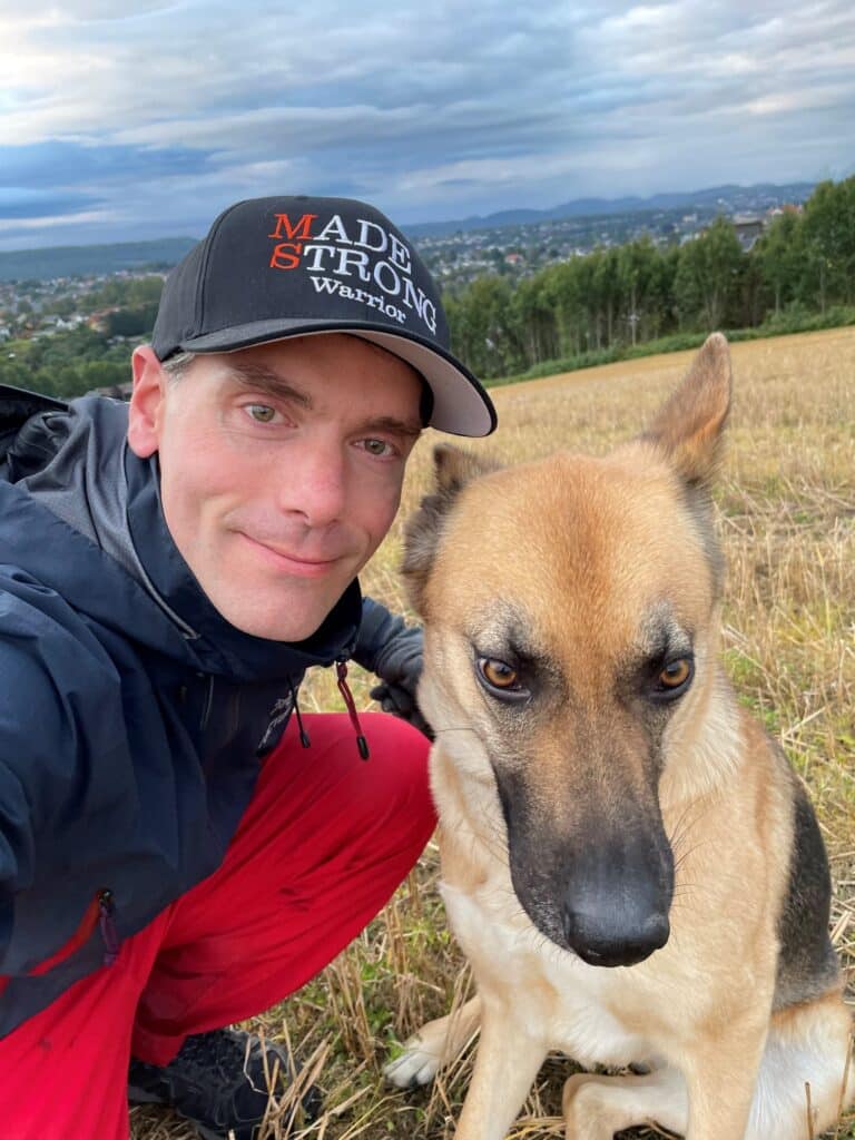 Bilde av Torbjørn Laundal og hans hund. I bakgrunn ser man et jorde og skog.