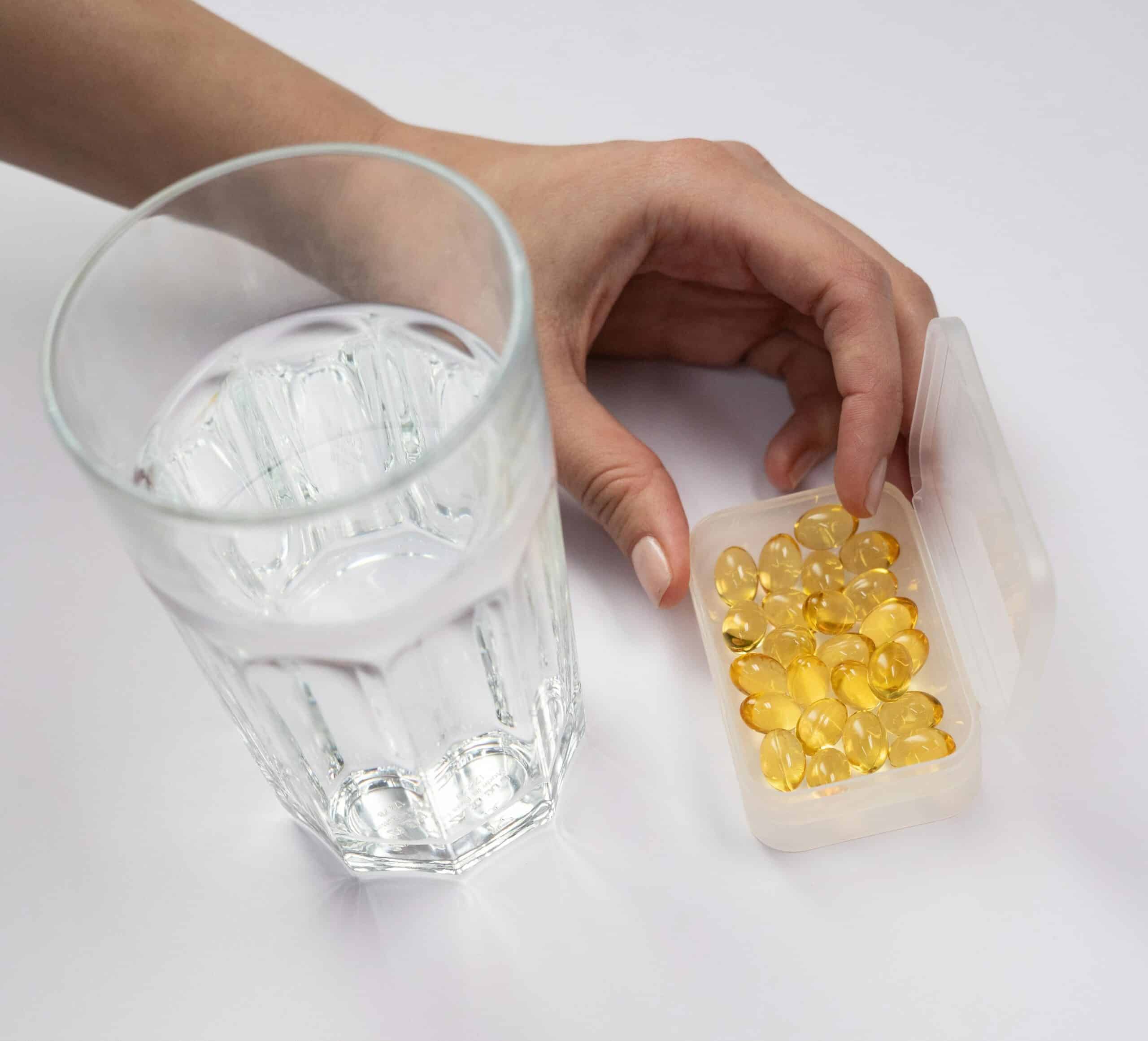 Bilde av en hånd som holder en boks med piller mens det står et vannglass ved siden av