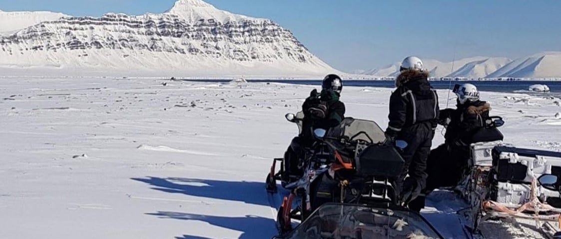 bilde fra svalbard med snø og fjell og tre menn på snøscooter