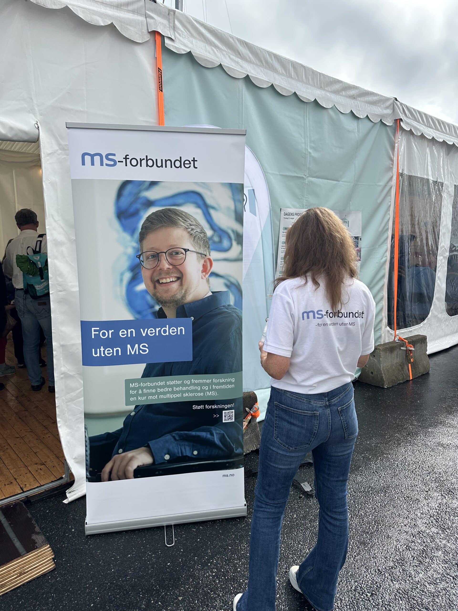 Bilde av MS-forbundet sin roll-up med en verden uten MS og ryggen til en ansatt med MS-forbundet t-skjorte